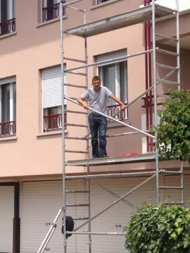 Peintre sur un échafaudage roulant devant la façade d’un immeuble