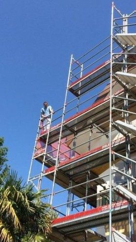 Peintre en haut d’un échafaudage monté contre une façade de plusieurs étages