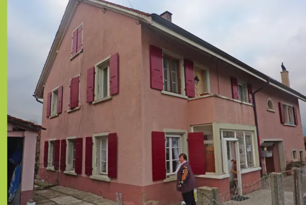 Maison de village rose aux volets rouges repeints