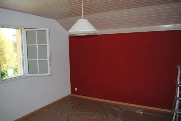 Pièce claire avec un mur peint en rouge profond et une suspension blanche