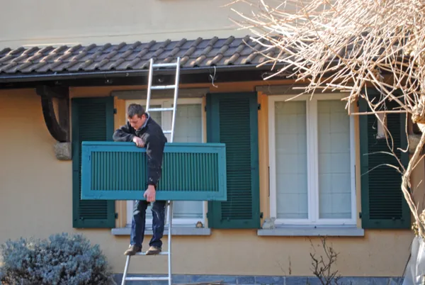 Peintre sur une échelle devant un volet repeint en bleu-vert