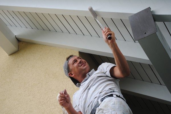 Artisan repeignant au rouleau la sous-face blanche d’un avant-toit